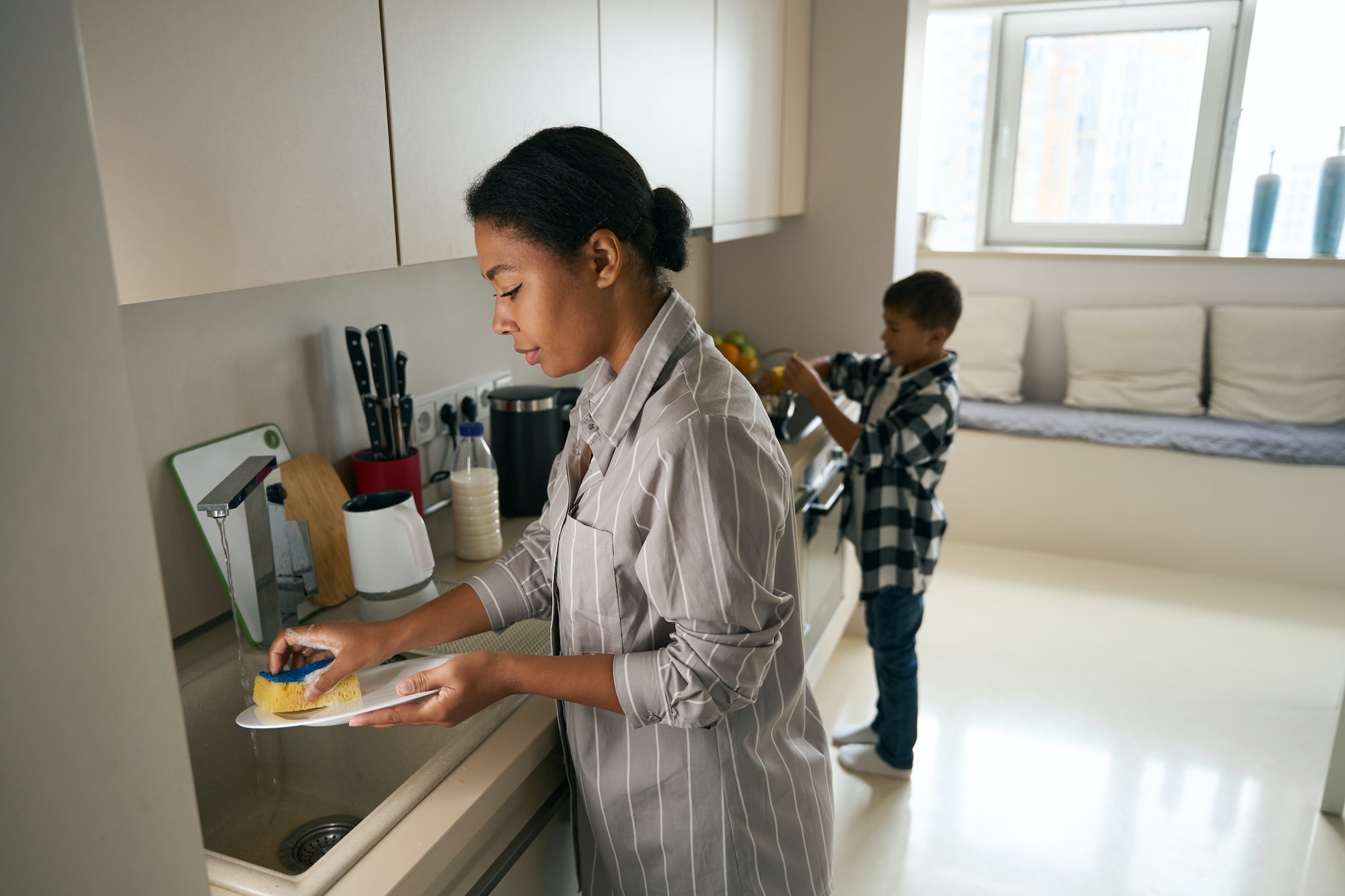 Beautiful elegant female is cleaning cuisine with son in the morning